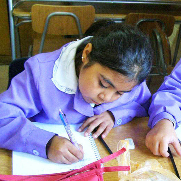 Fotografía de una niña en una aula escribiendo en una libreta.