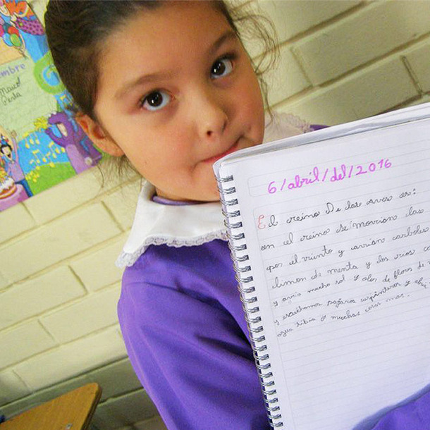 Fotografía de una niña en una aula sosteniendo una libreta.