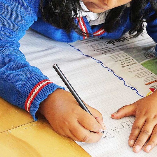 Niña con uniforme escolar de color azul escribiendo en su pupitre.