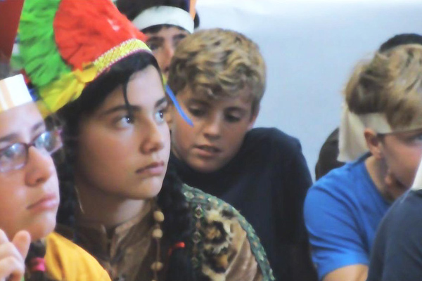 Niña con compañeros en un aula atendiendo en clase.