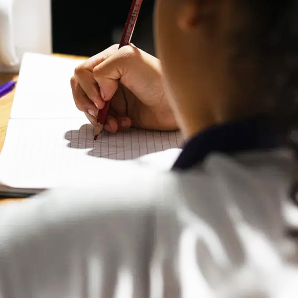 Niño de espaldas escribiendo en un cuaderno.